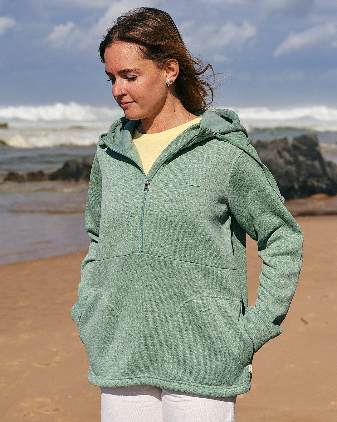 A woman standing on a beach wearing a Saltrock Galaksea - Womens 1/4 Zip Fleece - Light Green hoodie.