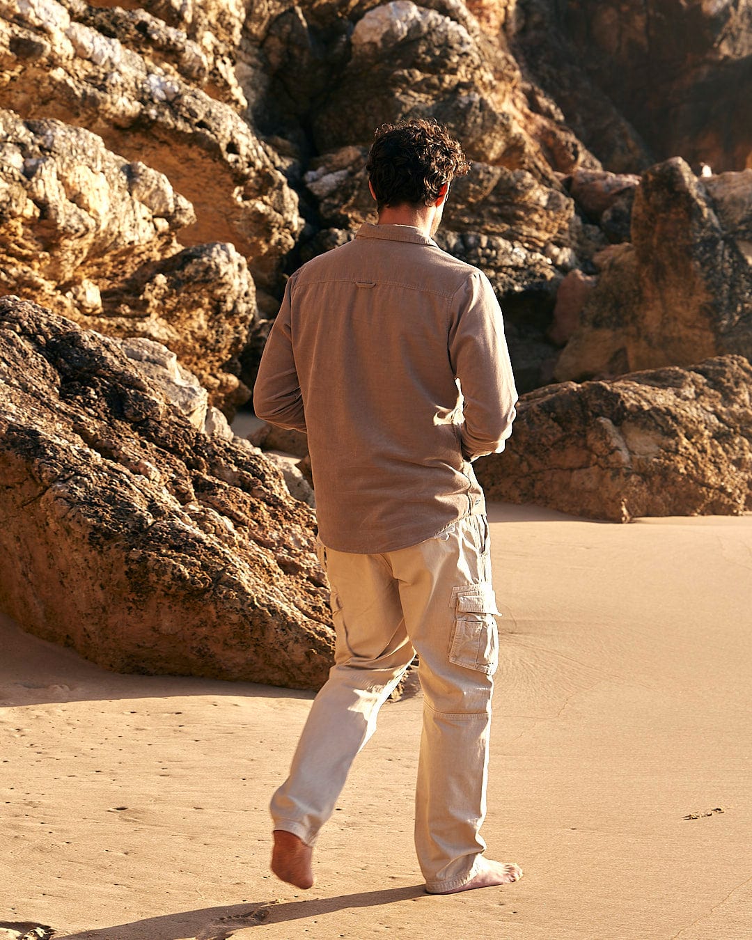 A man wearing Saltrock's Godrevy - Mens Cargo Trouser in Cream walks on the beach with a frisbee.