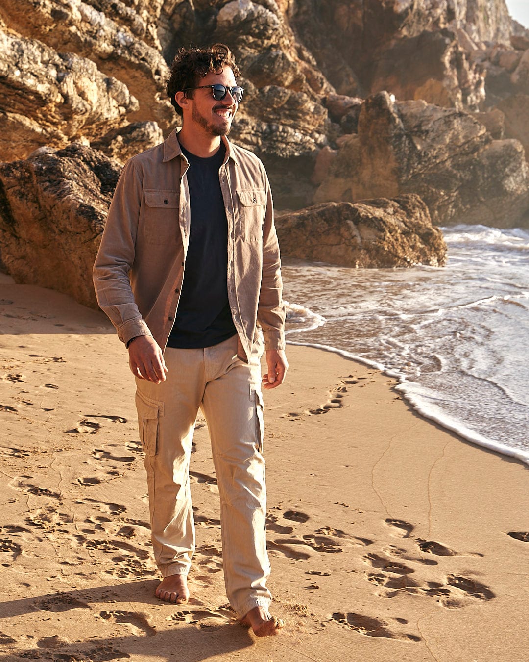 A man in Saltrock's Godrevy - Mens Cargo Trouser - Cream walking on a beach.