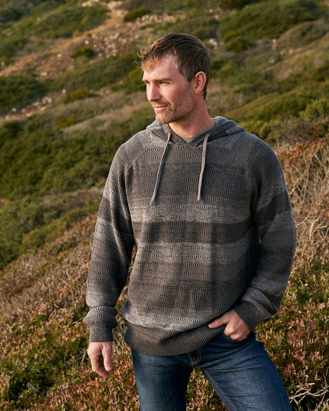 A man in a Saltrock Grohl - Mens Knitted Hoodie - Dark Grey standing on a hill.