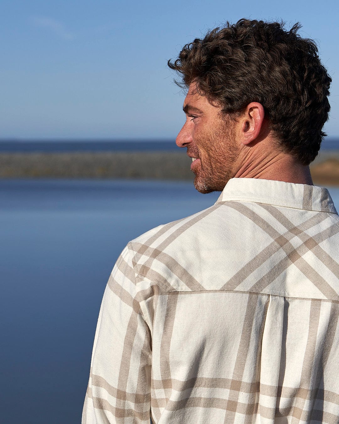 A man is standing by the water wearing a Saltrock Lazer - Mens Long Sleeve Check Shirt - Light Grey.