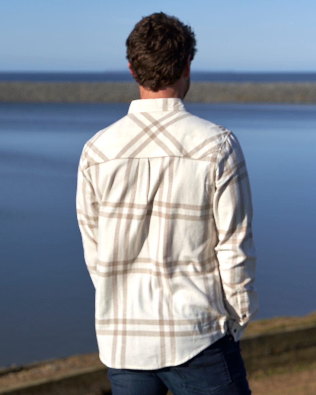 A man looking out over the water in a Saltrock Lazer - Mens Long Sleeve Check Shirt - Light Grey.