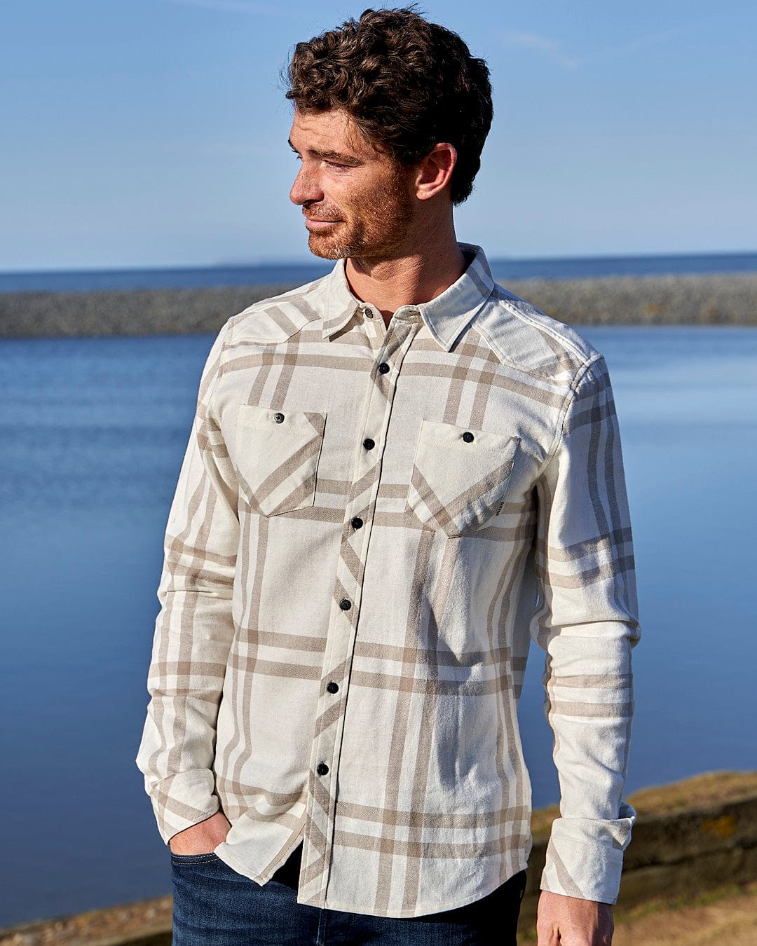 A man in a Saltrock plaid shirt standing by the water.