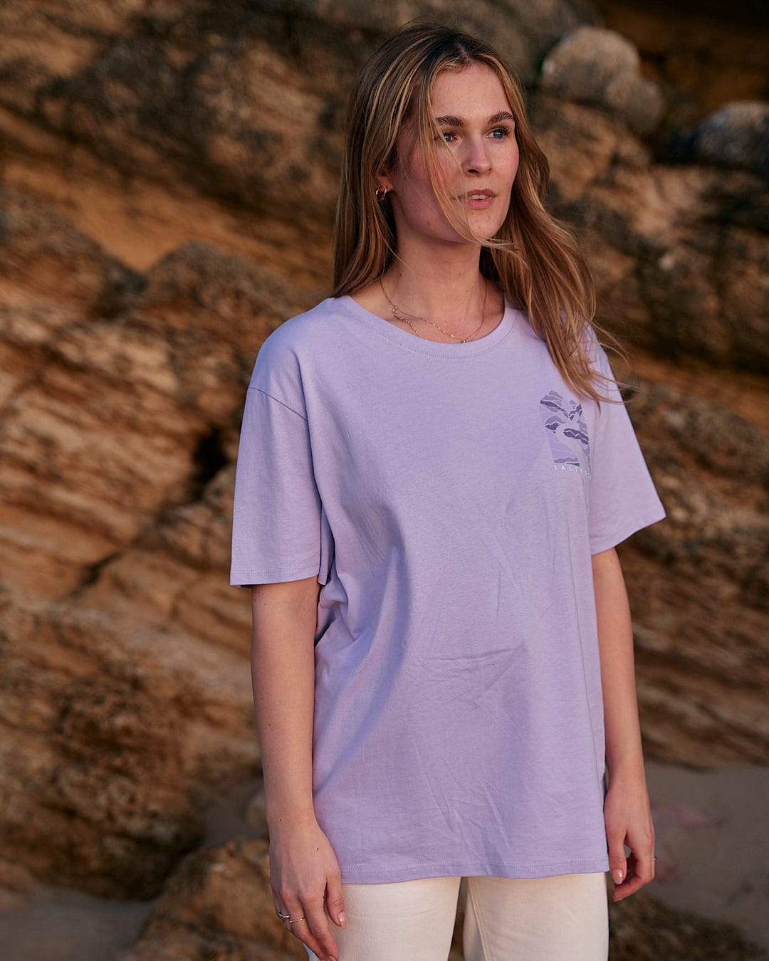 A woman wearing a Saltrock Live Wild - Womens Short Sleeve T-Shirt - Light Purple and white pants.