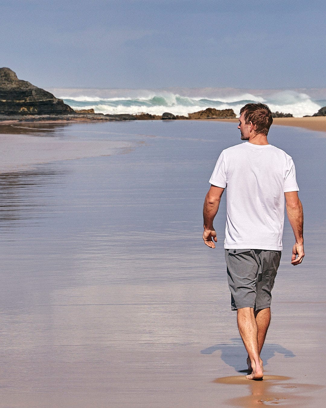 A man walking on a beach with a Lost At Sea Skull - Mens Short Sleeve T-Shirt - White by Saltrock.