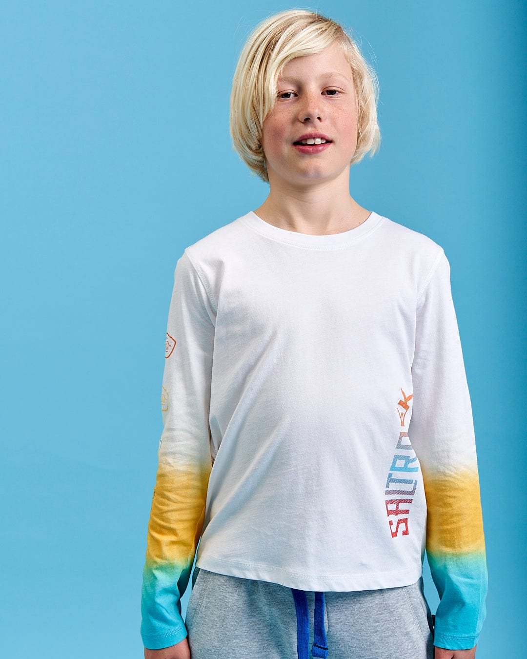 A young boy wearing a Saltrock Marcus - Kids Long Sleeve Dip Dye T-Shirt - White.