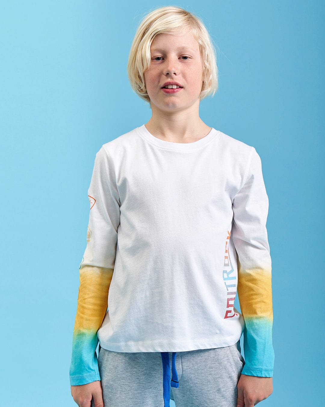 A young boy wearing a Saltrock Marcus - Kids Long Sleeve Dip Dye T-Shirt in white.