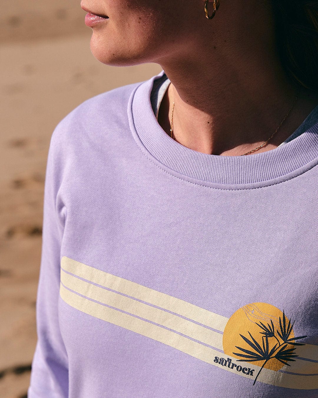 A woman wearing a Saltrock Poster Stripe - Womens Crew Sweat - Light Purple sweatshirt with a palm tree on it.
