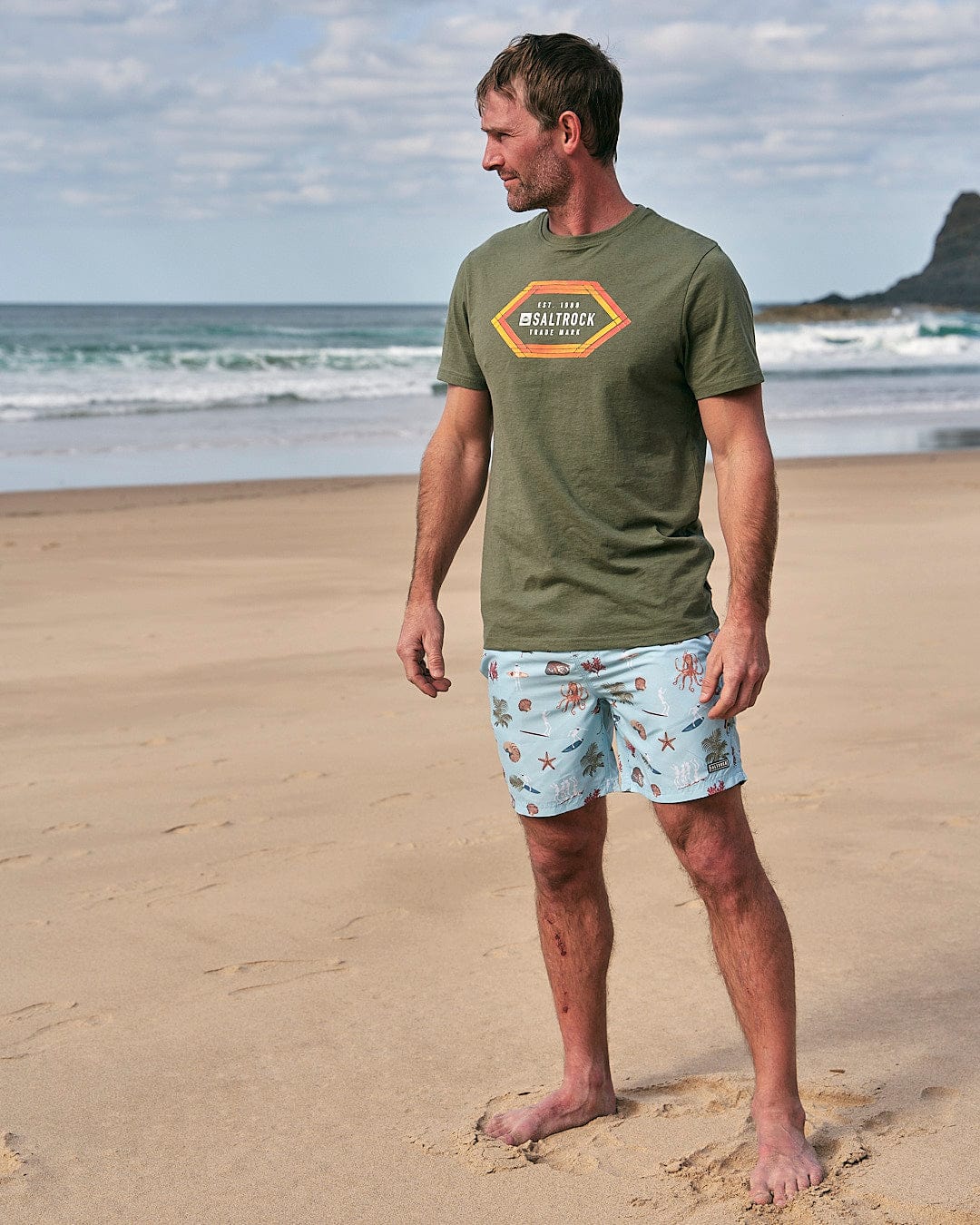 A man standing on the beach wearing Saltrock Ruan - Mens Swimshorts - Light Blue.