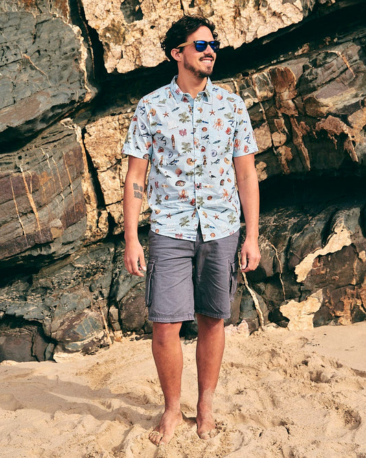 A man exuding holiday vibes, standing on the beach wearing a Saltrock Ruan - Mens Washed Short Sleeve Shirt.