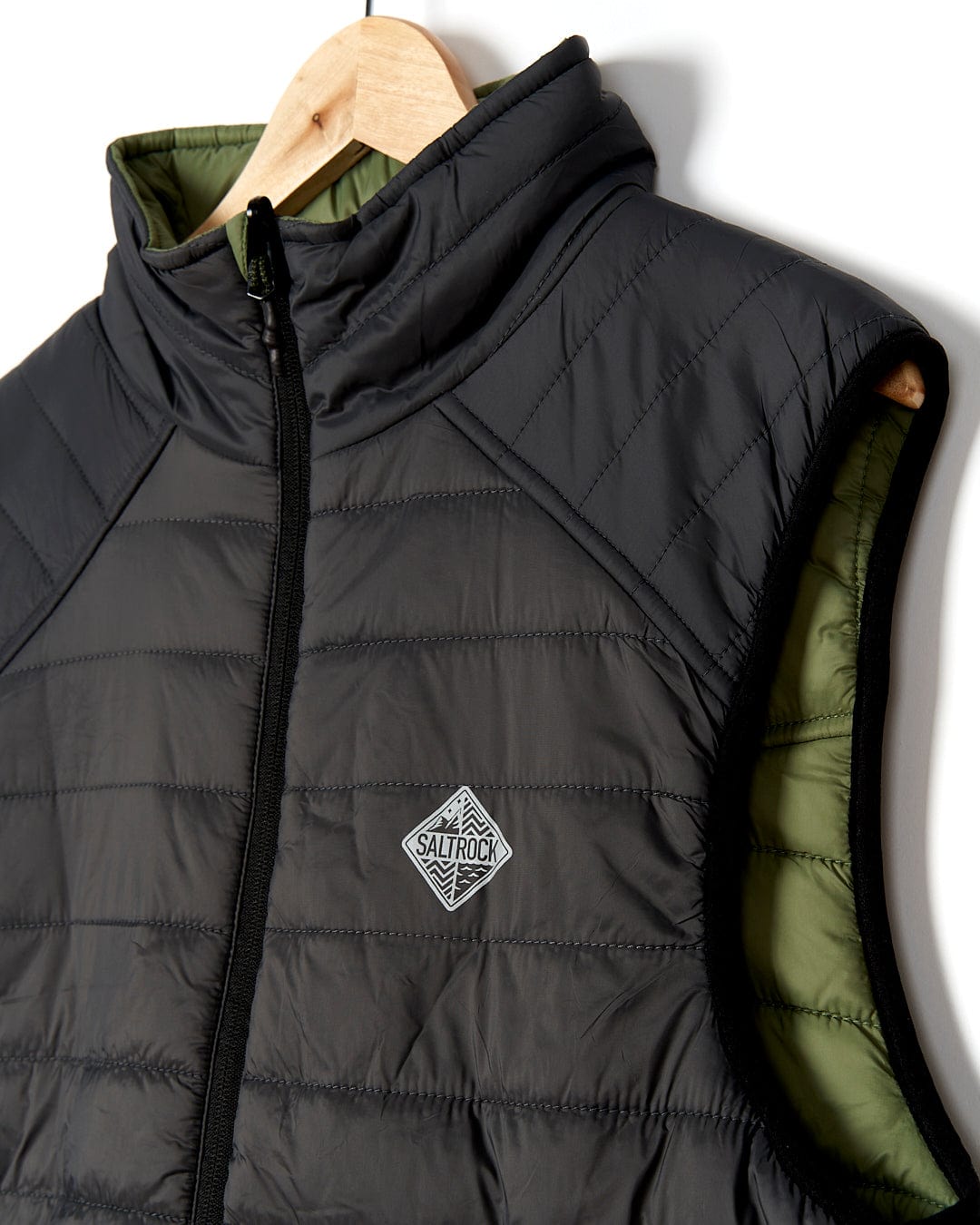 A Saltrock - Scott Mens Reversible Gilet - Dark Green/Black hanging on a hanger.
