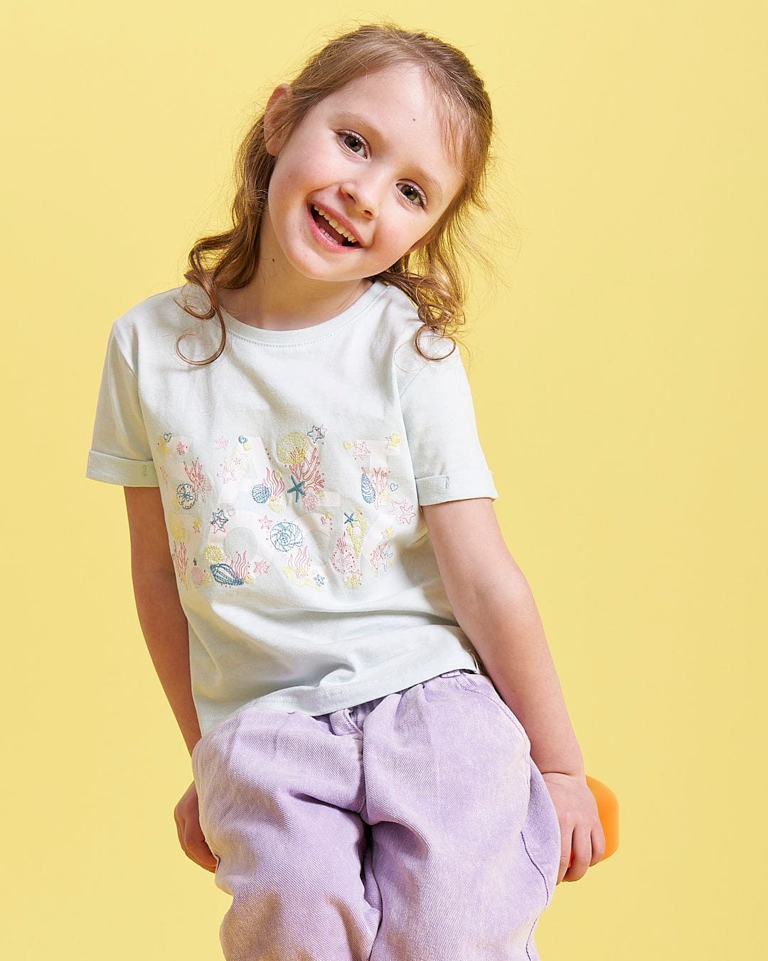 A girl sitting on a Seabed - Kids Short Sleeve T-Shirt - Light Blue chair from Saltrock.