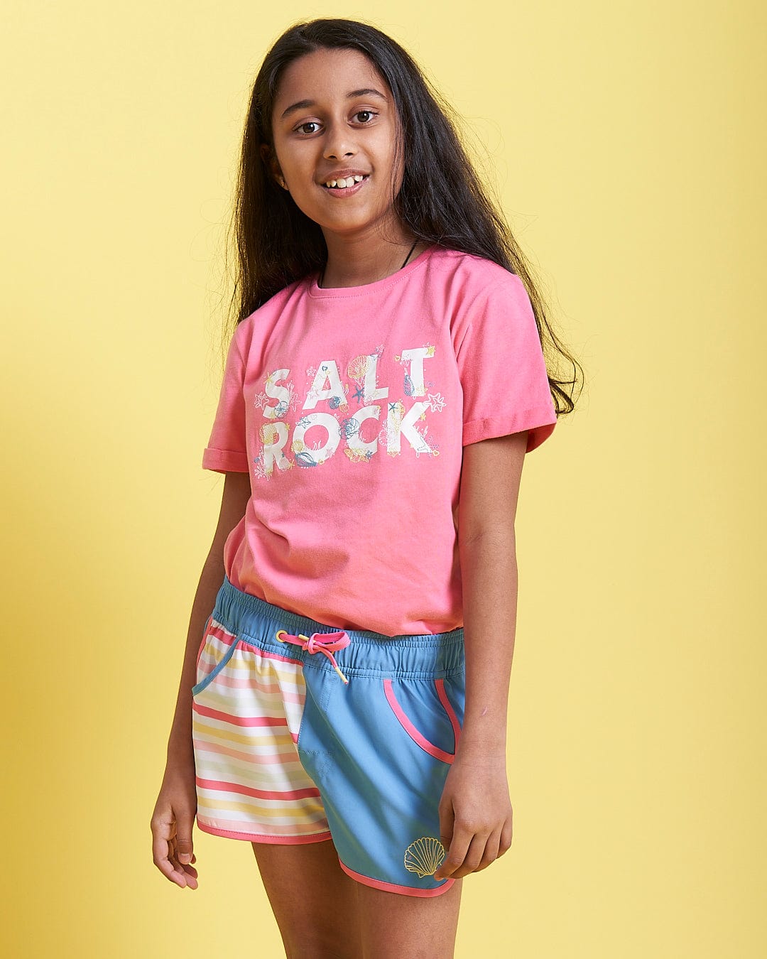 A girl in a Saltrock Seabed - Kids Short Sleeve T-Shirt - Pink and shorts.