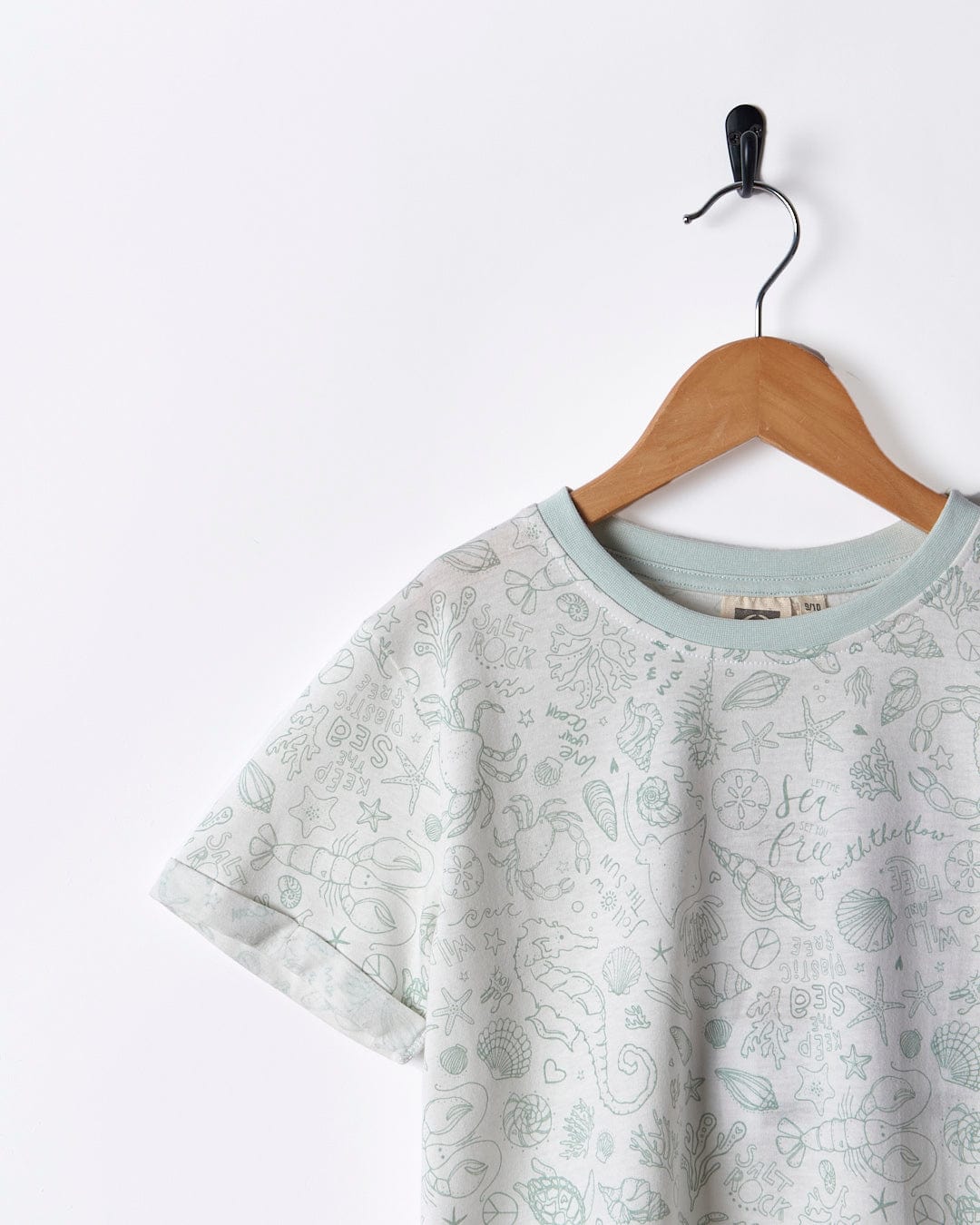 A Saltrock Seashore - Kids All Over Print Short Sleeve T-Shirt - White hanging on a hanger.