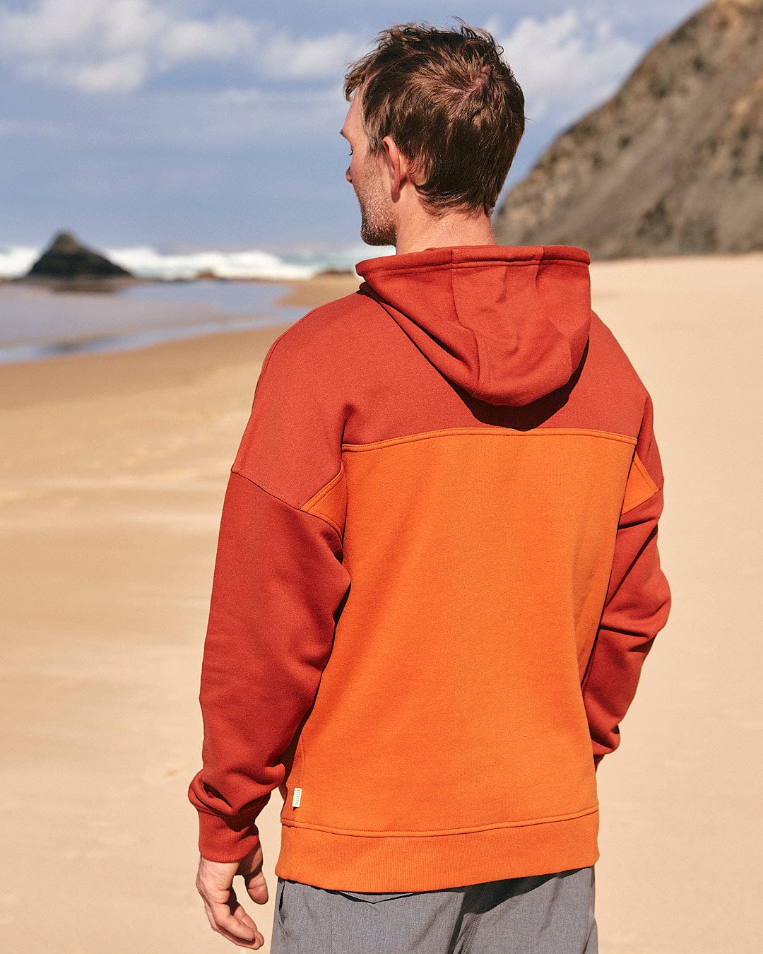 A man is standing on the beach wearing a Saltrock Speed Embroidery - Mens 1/4 Neck Zip - Red hoodie.