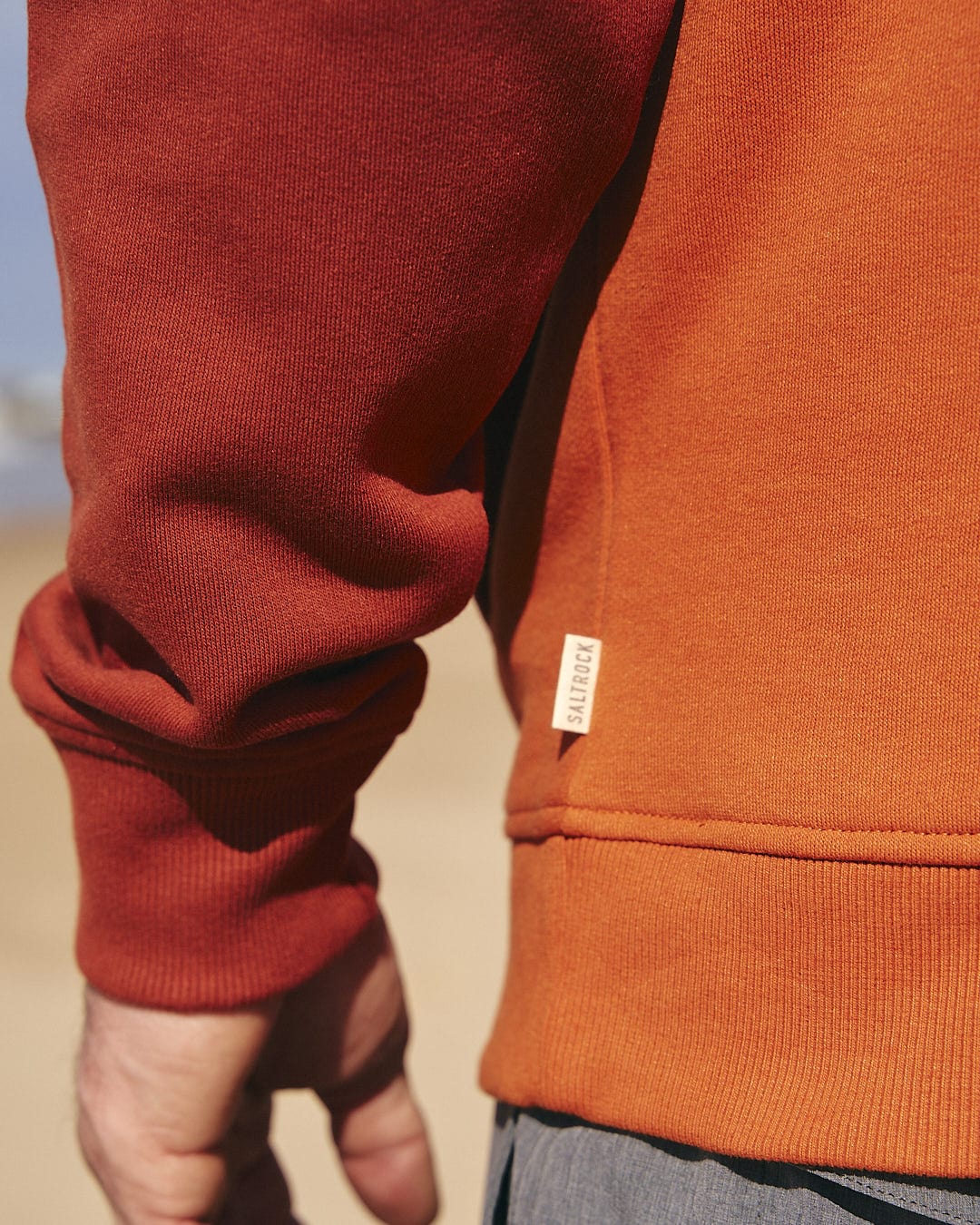 A man wearing a Saltrock Speed Embroidery - Mens 1/4 Neck Zip - Red sweatshirt on the beach.