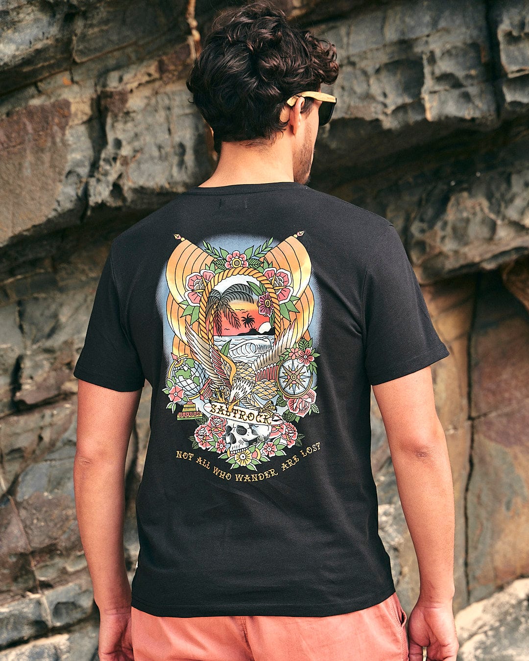 The back of a man wearing Saltrock's Tattoo Island - Mens Short Sleeve T-Shirt - Black and sunglasses.