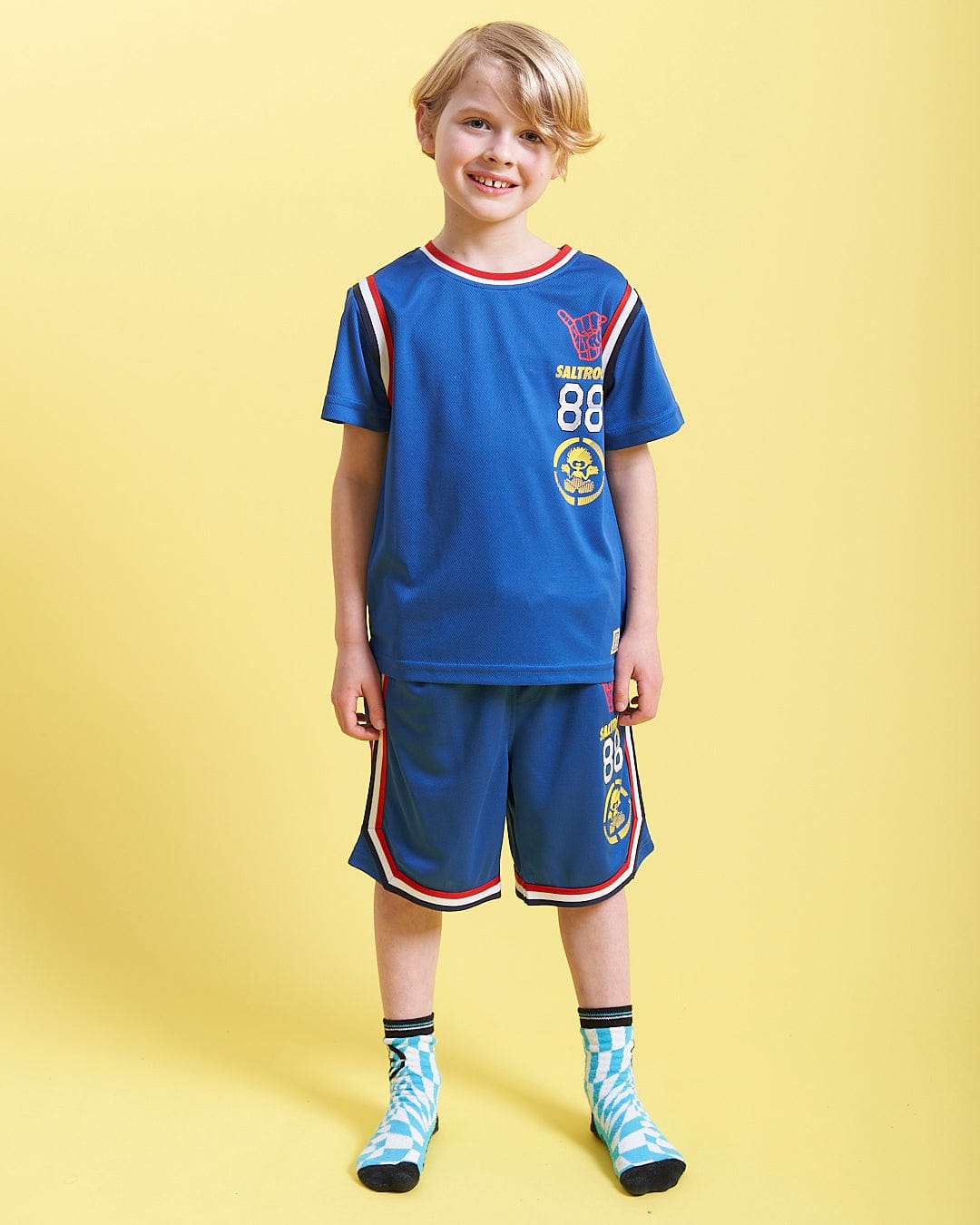 A young boy wearing a Saltrock Team - Kids Short Sleeve T-Shirt - Blue and shorts.