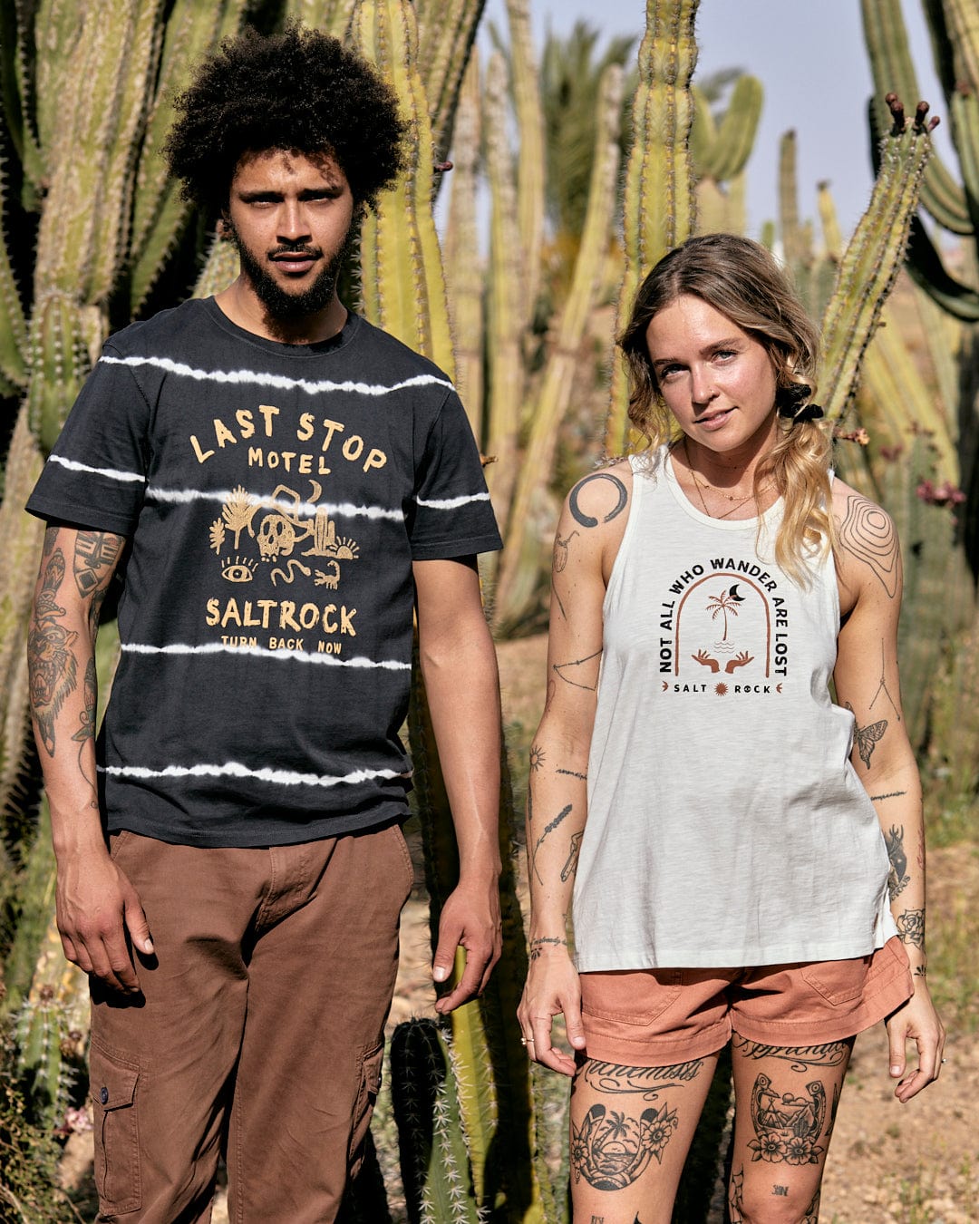A man and a woman standing in a desert landscape, both wearing Saltrock Palmera - Womens Vest - White outfits made of 100% cotton and surrounded by tall cacti.