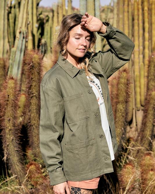 A woman in a Saltrock Barden - Womens Lightweight Utility Jacket in Dark Green stands in front of tall cacti, shielding her eyes from the sun with her hand.