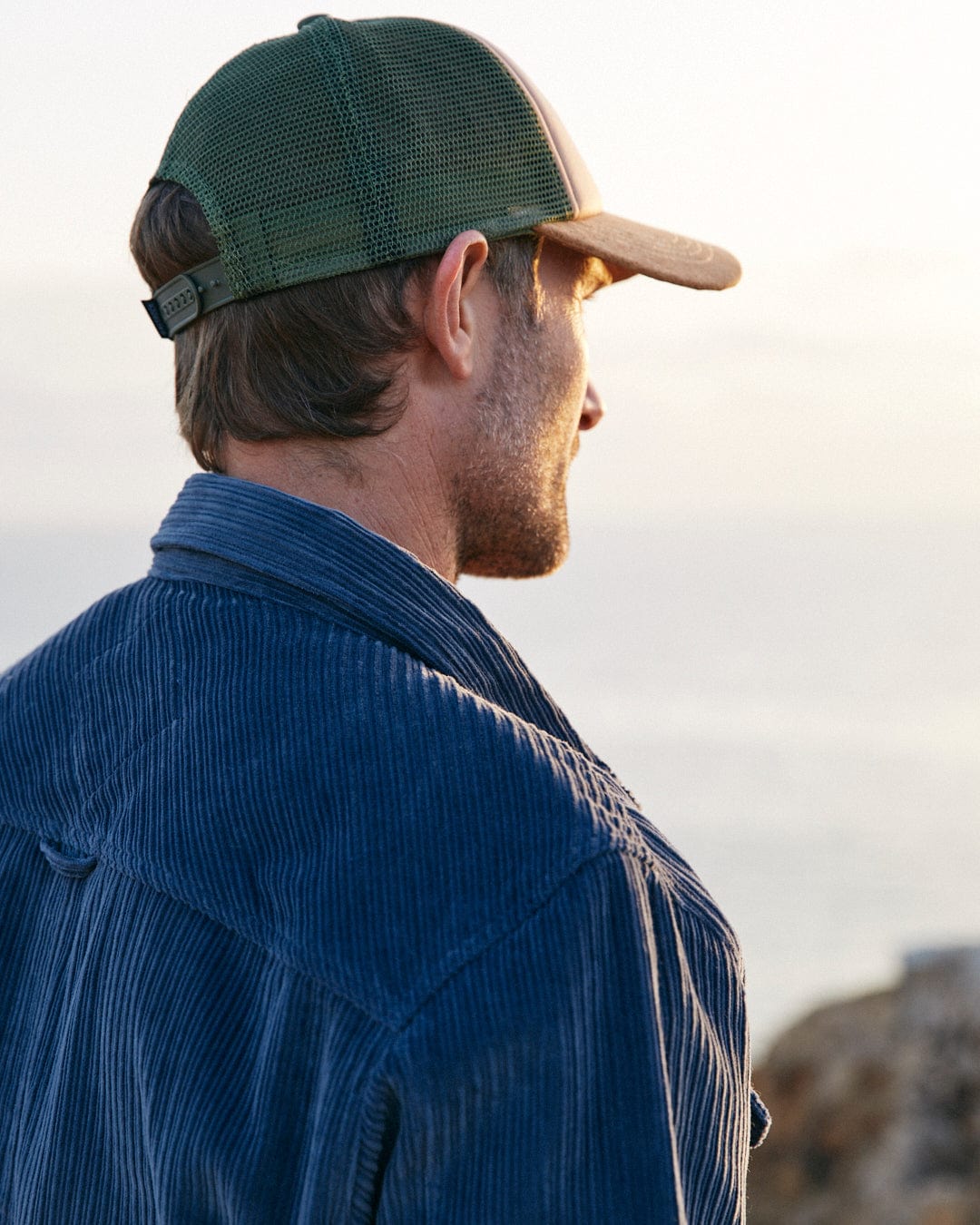 A man wearing a Saltrock Ace - Mens Long Sleeve Shirt in Blue with front chest pockets and a hat looking out over the ocean.