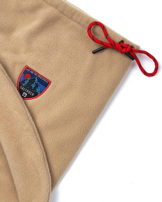 An adjustable Patchy - Borg Snood - Beige fleece blanket with a red badge on it. Brand: Saltrock