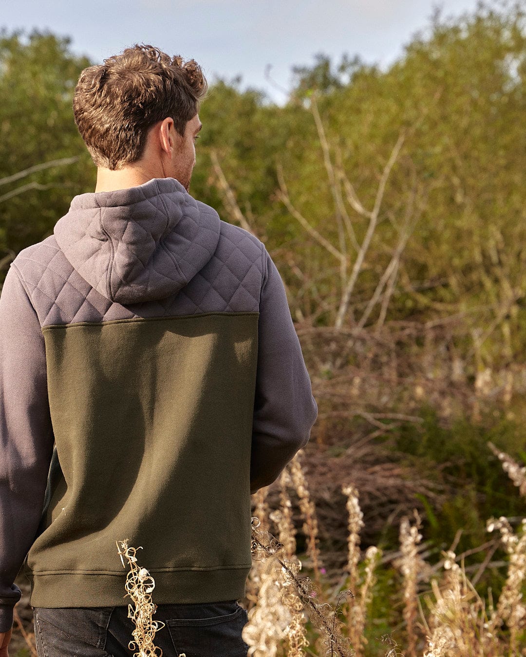 A Saltrock Aiken Mens 1/4 Neck Hoodie - Green provides warmth and comfort for a man standing in the outdoors field.