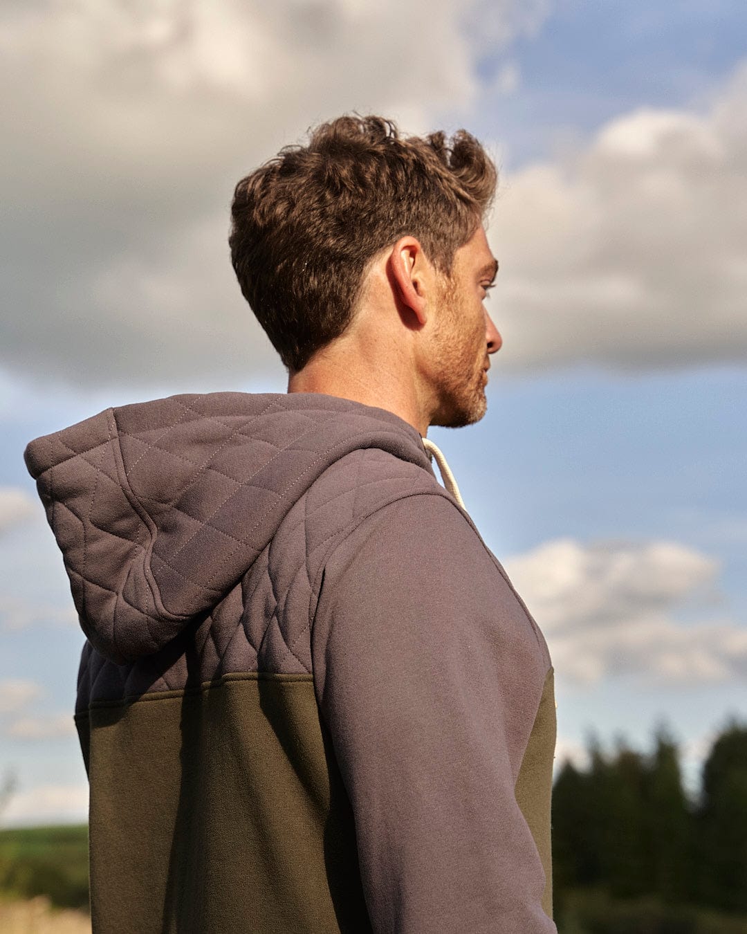 A man in a Saltrock hoodie feeling warmth and comfort while looking out over a field wearing the Aiken - Mens 1/4 Neck Hoodie - Green.