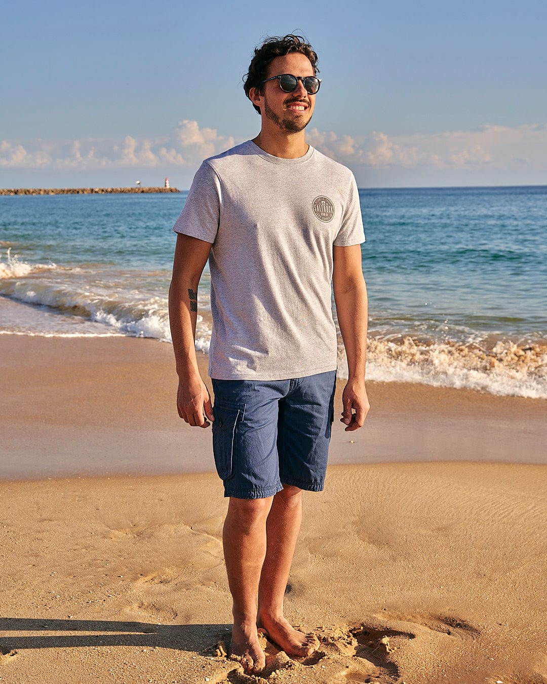 A man standing on a beach wearing the All Terrain - Mens Short Sleeve T-Shirt - Grey by Saltrock.