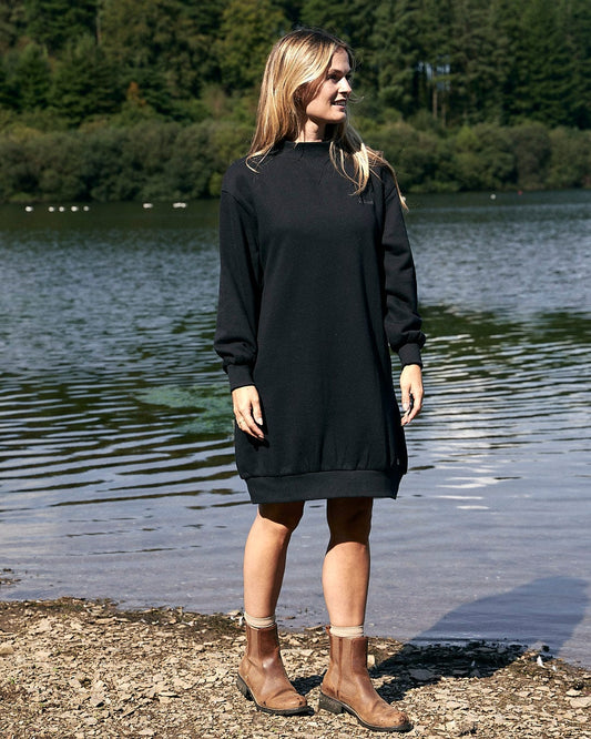 A woman in a Saltrock black dress standing by a body of water.