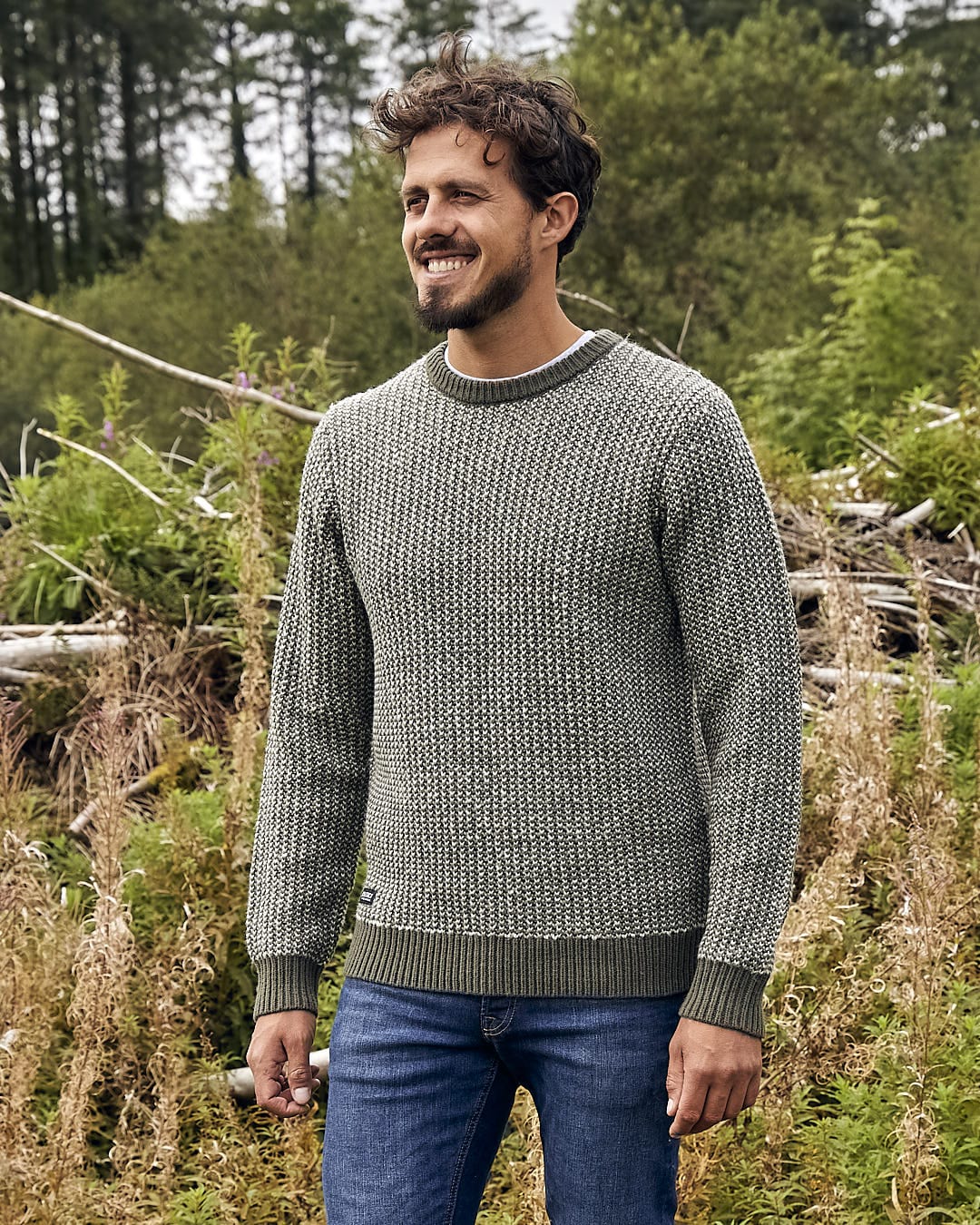 A man is standing in a field wearing the Saltrock Arlen - Mens Crew Knit - Dark Green sweater.