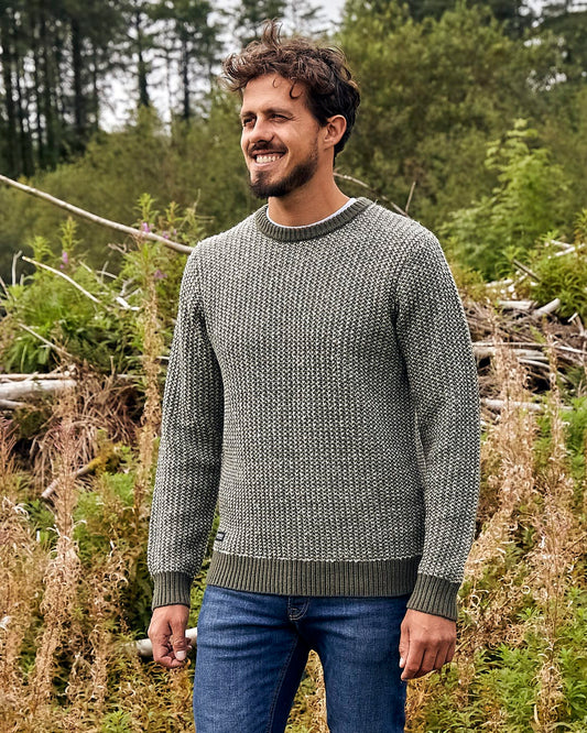 A man is standing in a field wearing the Saltrock Arlen - Mens Crew Knit - Dark Green sweater.
