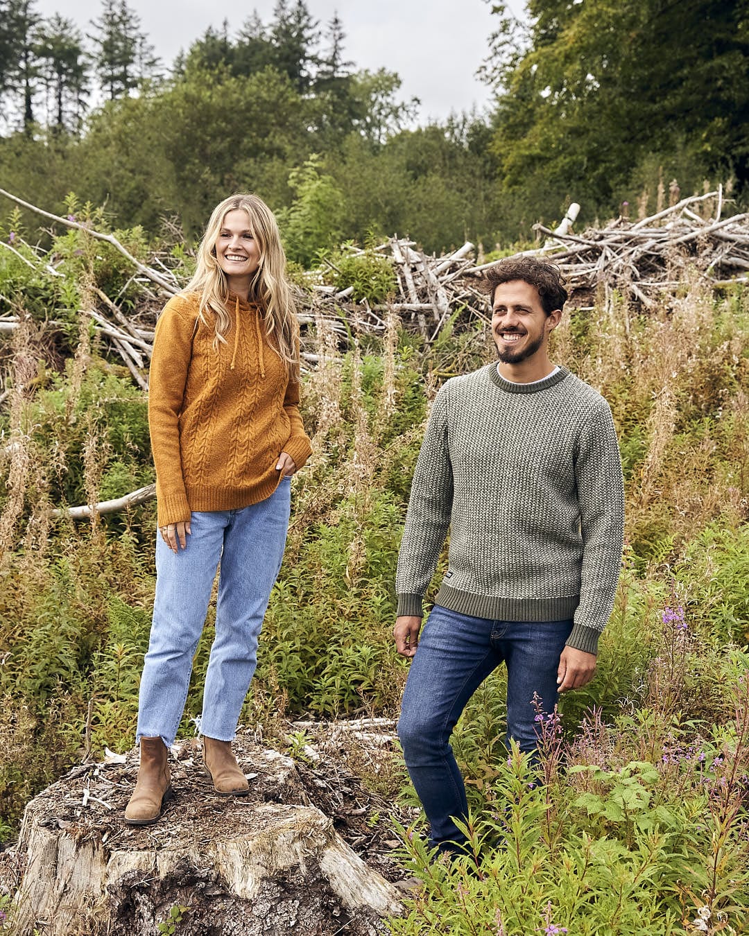 A man and woman standing on top of a log in the woods, wearing the Arlen - Mens Crew Knit - Dark Green by Saltrock.