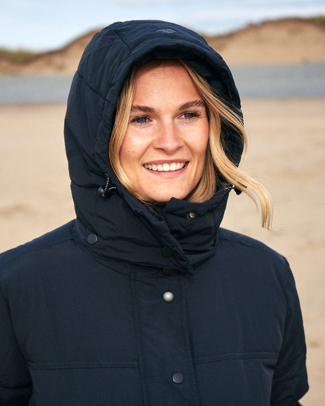 A woman wearing a Saltrock Aspen - Womens Short Puffer Jacket - Black on the beach during winter outdoor activities.