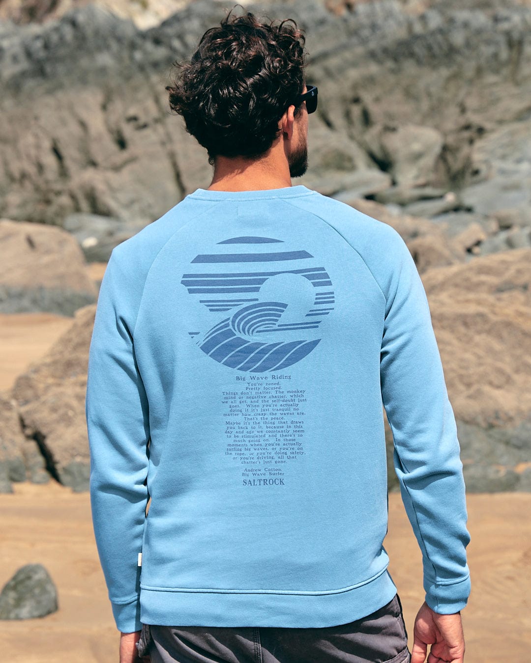 The back of a man wearing a Saltrock Atlantic - Mens Crew Sweat - Light Blue on the beach.