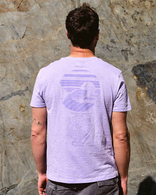 A man wearing the Saltrock Atlantic - Mens Short Sleeve T-Shirt in Purple standing in front of a rock wall.