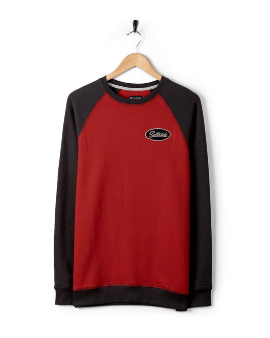 A red and black raglan contrast sleeves sweatshirt with a logo on the chest, hanging on a wooden hanger against a white background. (Product Name: Attendant - Recycled Mens Sweat - Red, Brand Name: Saltrock)