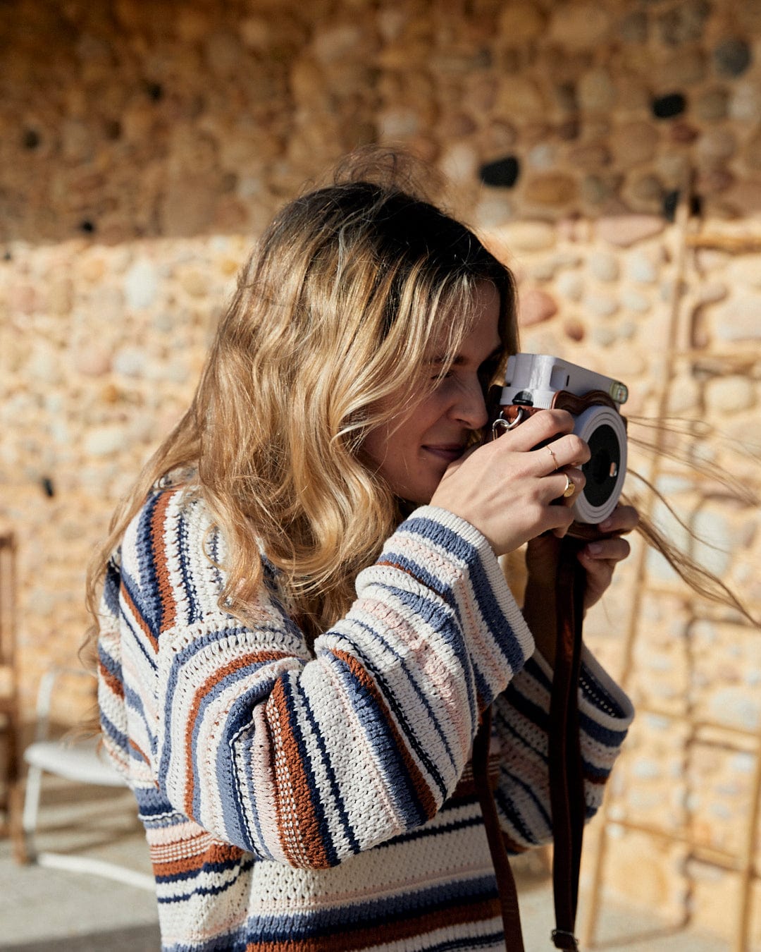 A woman snapping a photo with the Saltrock Aubrey Pop - Womens Hooded Crochet Knit - Cream in front of a stone wall.