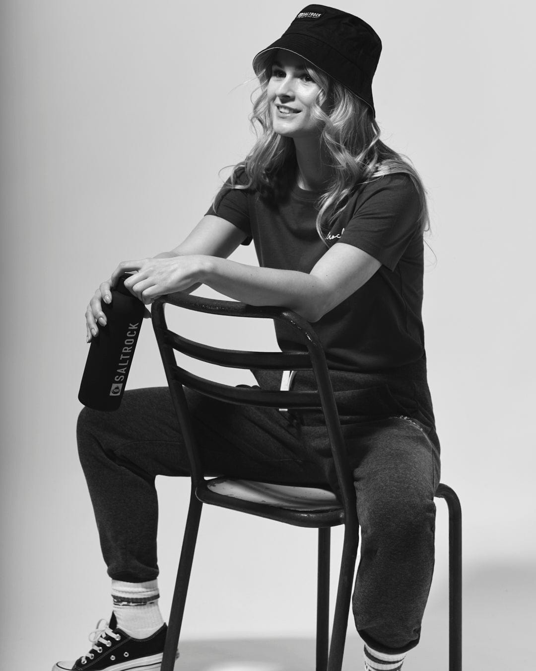 A black and white photo of a woman sitting on a chair wearing the Saltrock Velator Women's Short Sleeve T-Shirt in Navy, in a core classic style.