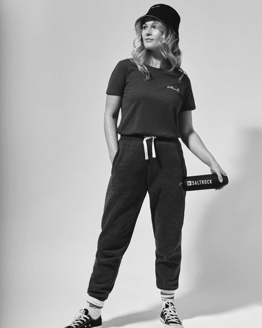 Woman in casual attire with Saltrock Velator joggers in Dark Grey, cap, and clutch bag posing for a monochrome fashion photograph.