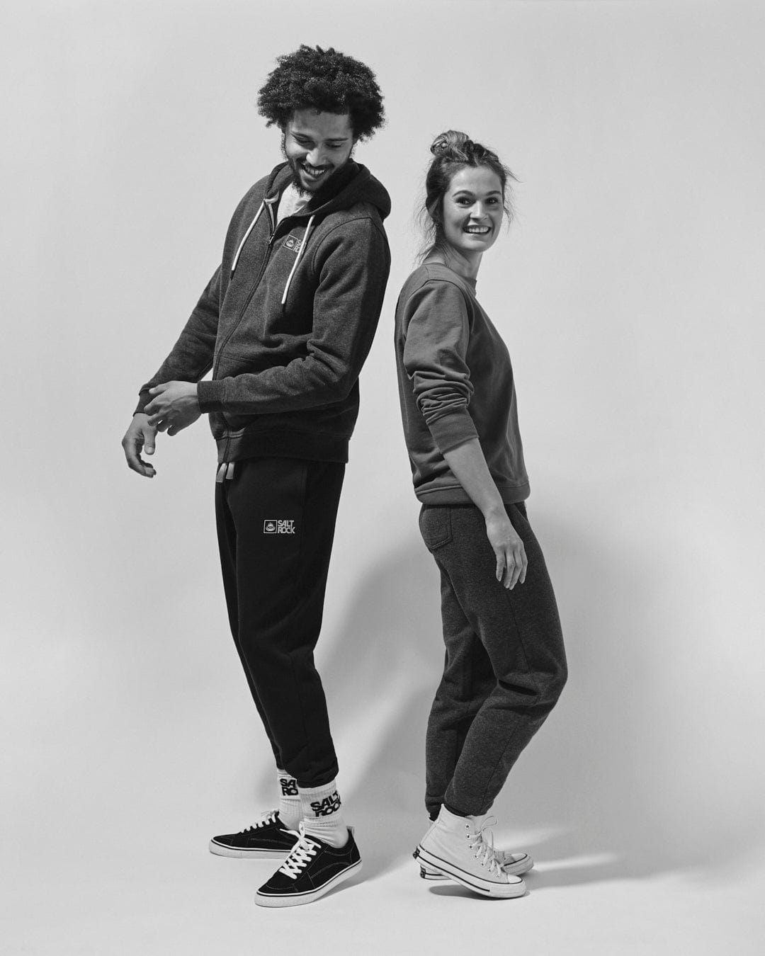 A black and white photo of a man and woman posing for a photo, both wearing hoodies with Saltrock Original - Mens Zip Hood - Dark Grey branding.