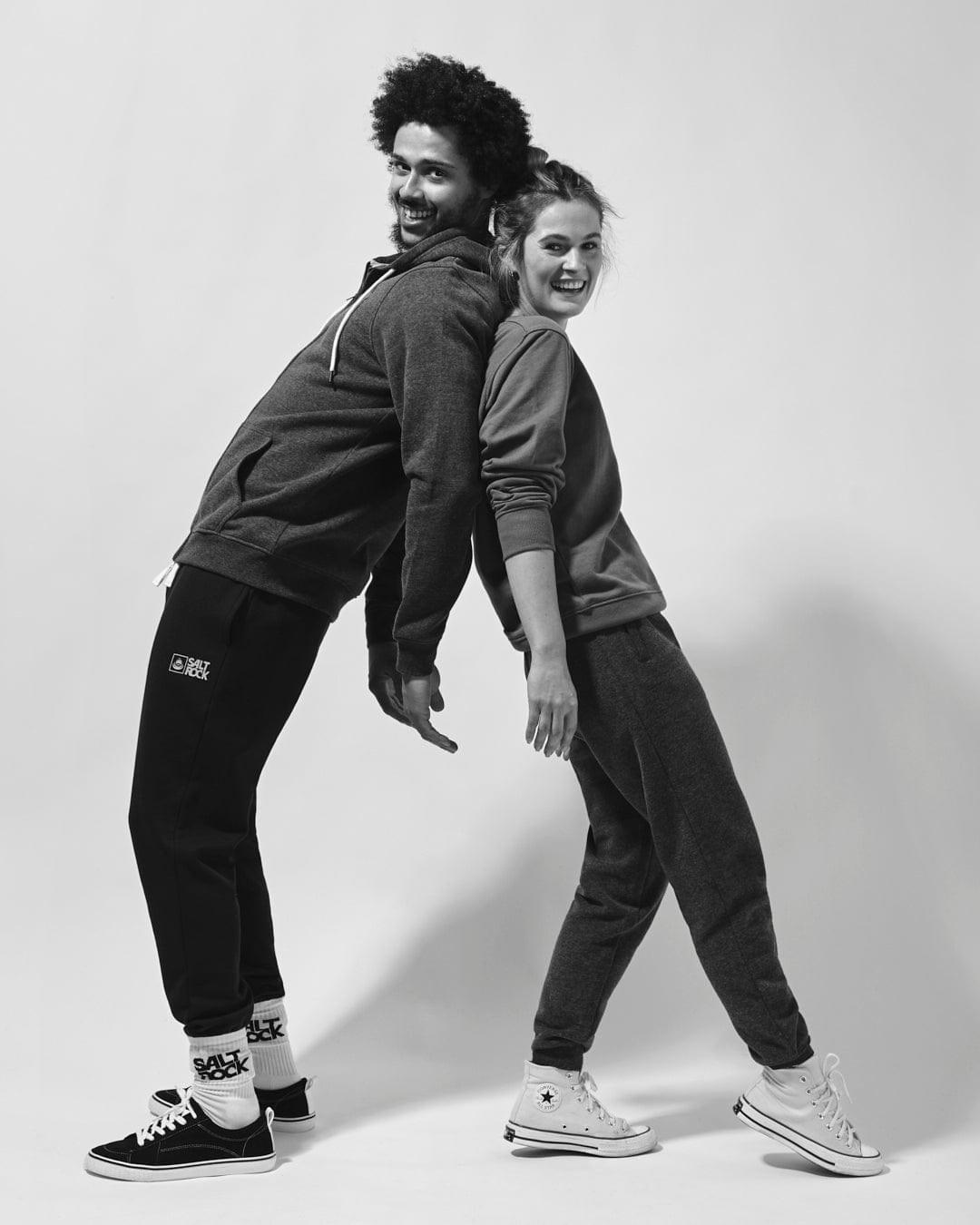 Two people smiling and standing back-to-back in casual attire with cuffed ankles wearing the Saltrock Velator Womens Joggers in Dark Grey.