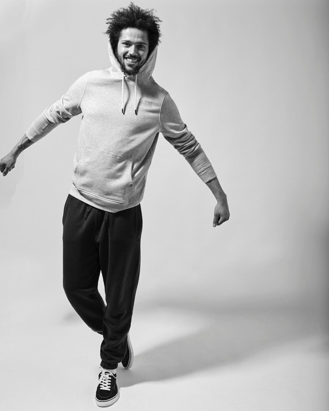 A man in a Saltrock Original - Mens Pop Hoodie - Grey smiles while posing in a mid-step with one foot slightly lifted, against a plain background.
