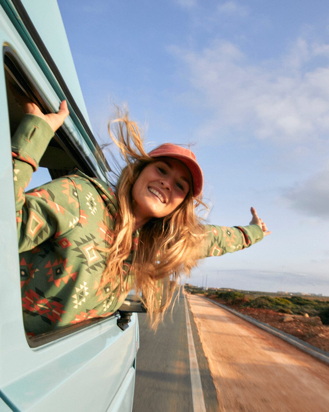 Woman enjoying a road trip, leaning out of a van window with a joyful expression, wearing Aztec Santano - Womens Pop Hoodie in Green/Orange by Saltrock.