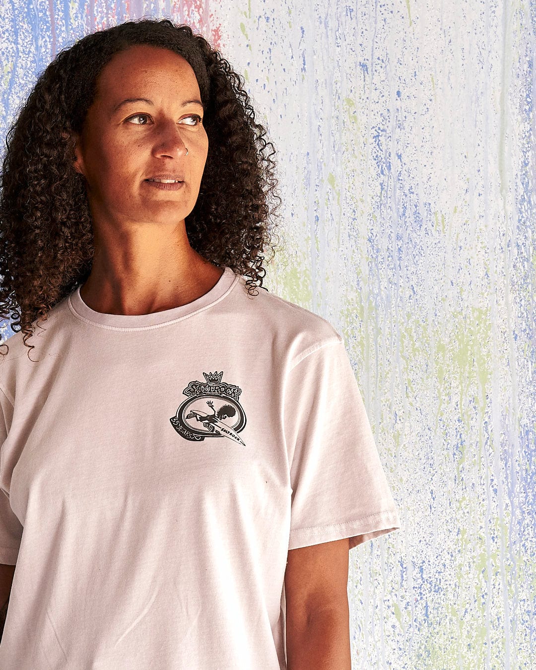 A woman with curly hair wearing a Saltrock Balls To The Wall - Limited Edition 35 Years T-Shirt.