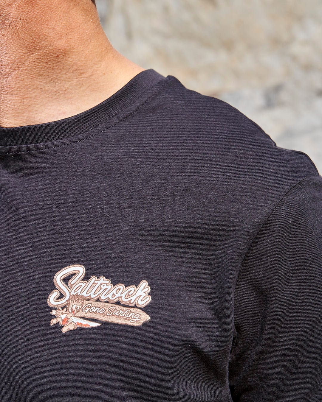 A man wearing a Saltrock Beach Sign Devon - Mens T-Shirt - Dark Grey with a logo on it.