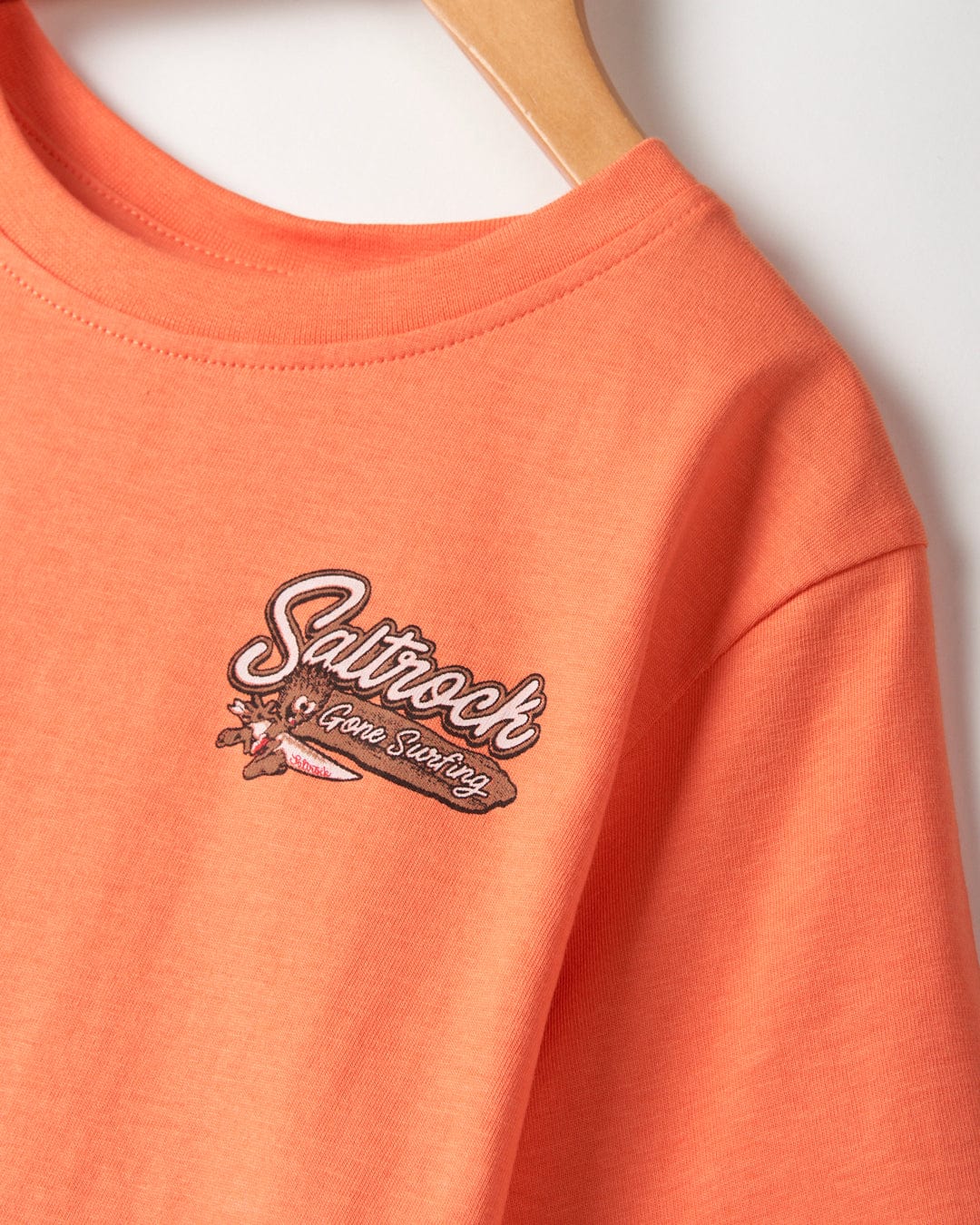 A machine washable Beach Signs Devon - Kids Short Sleeve T-Shirt in orange with a Saltrock branding logo on it.