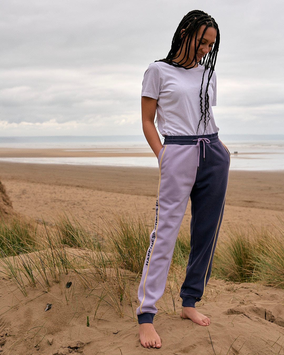 A woman in a Betty - Womens Jogger - Light Purple t-shirt standing on a sand dune by Saltrock.
