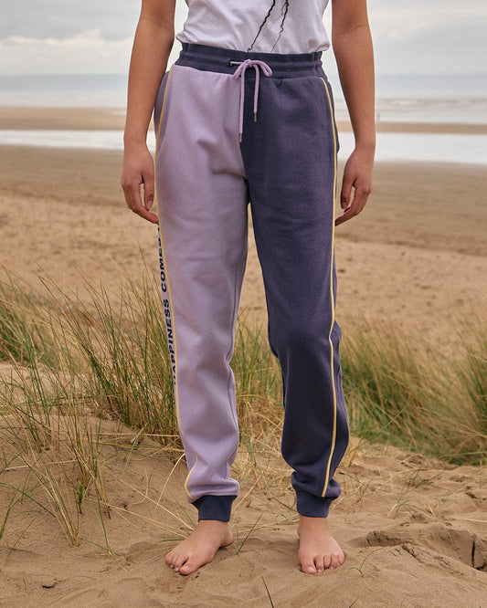 A woman standing on a beach wearing Saltrock Betty - Womens Jogger - Light Purple sweatpants.