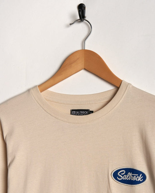 Cream long-sleeve t-shirt on a wooden hanger against a white background, featuring the "Saltrock" badge on its chest.